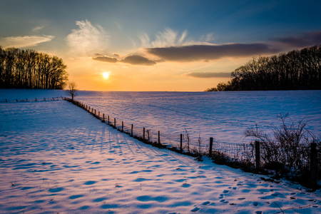 Winter sunset over a fence and snow covered farm field in rural Carroll County, Maryland.の写真素材