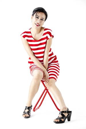 Asian woman in red stripes dress posing on a stoolの写真素材