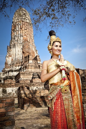Asian woman dressed in traditional Thai attire standing in front of a historical structureの写真素材