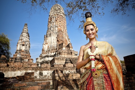 Asian woman dressed in traditional Thai attire standing in front of a historical structureの写真素材