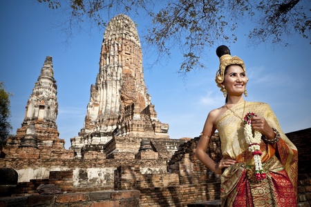 Asian woman dressed in traditional Thai attire standing in front of a historical structureの写真素材