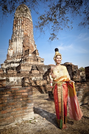 Asian woman dressed in traditional Thai attire standing in front of a historical structureの写真素材
