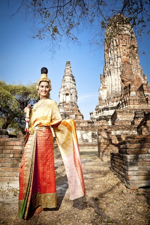 Asian woman dressed in traditional Thai attire standing in front of a historical structureの写真素材
