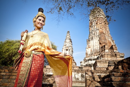 Asian woman dressed in traditional Thai attire standing in front of a historical structureの写真素材
