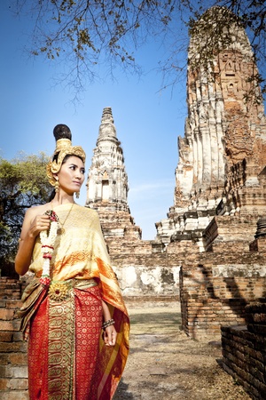 Asian woman dressed in traditional Thai attire standing in front of a historical structureの写真素材