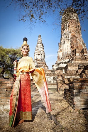 Asian woman dressed in traditional Thai attire standing in front of a historical structureの写真素材