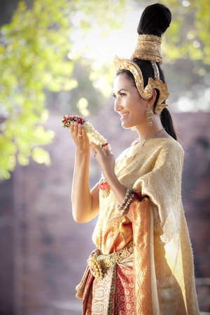 Asian woman dressed in traditional Thai clothing posing with a flowerの写真素材