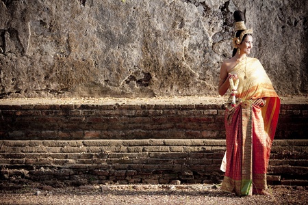 Woman dressed in traditional Thai attire posing in front of a wallの写真素材