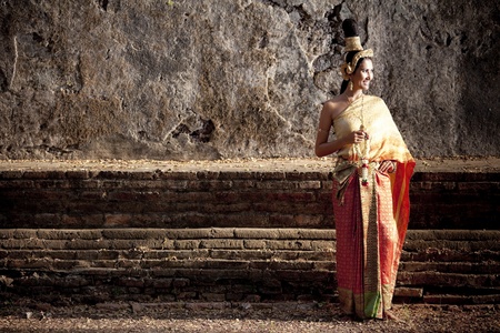 Woman dressed in traditional Thai attire posing in front of a wallの写真素材