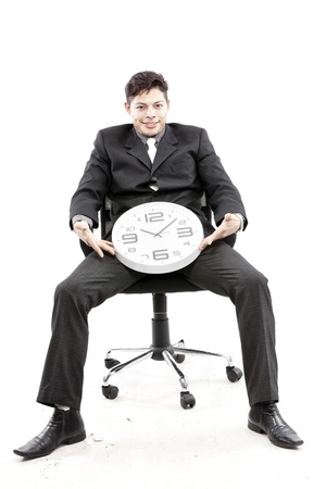 Portrait of a businessman sitting and a clock between his leg against white backgroundの写真素材