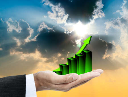 Businessman s hand holding a bar graph with sky at the backの写真素材