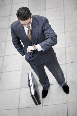 Businessman is looking at his watch with his briefcaseの写真素材