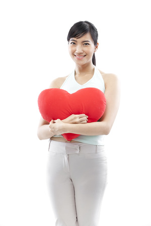 Young woman hugging a heart shaped cushion and smiling at the cameraの写真素材