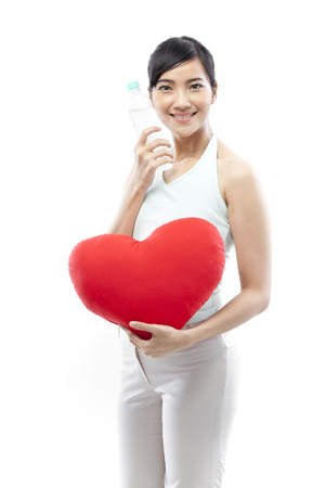 Young woman holding a heart shaped cushion and a water bottleの写真素材