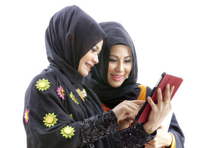 Women wearing hijab and dressed in malay attire while holding a stack of books and looking at a...