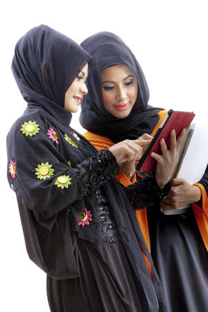 Women wearing hijab and dressed in malay attire while holding a stack of books and looking at a tabletの写真素材