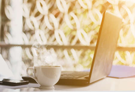 Hot coffee, Laptop and mobile on the table in bright morning.の写真素材
