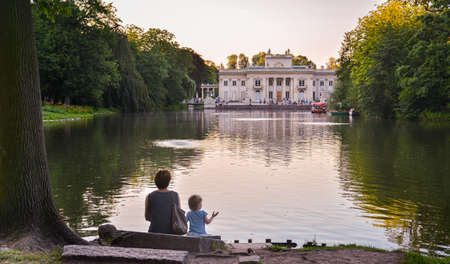 A woman and a little girl are sitting at the pond looking at the palace in Lazienkiのeditorial素材