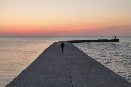 Silhouette of a man walking on the pier at sunset.の写真素材