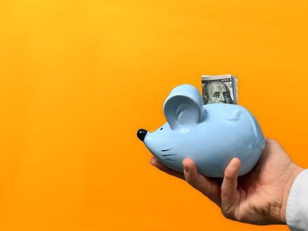 Blue piggy bank with dollar banknote in hand on orange backgroundの写真素材