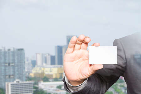 businessman holding visit card in hand and standing with building, business idea concept