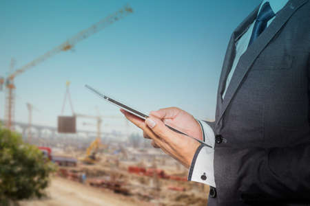Businessman holding a tablet computer blurred of construction site backgroundの写真素材