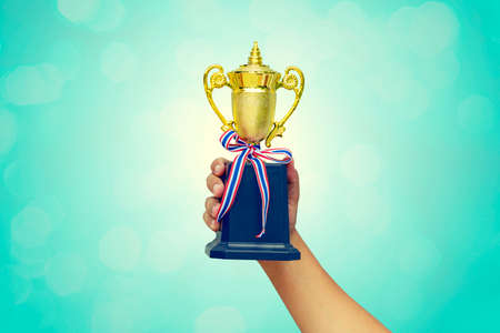 Hand holding up a gold trophy cup as a winner in a competitionの写真素材