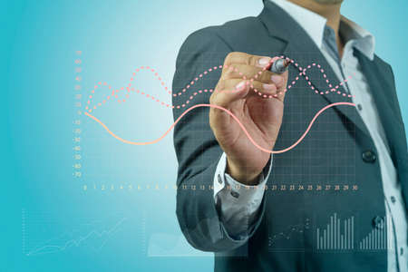 Businessman drawing graphics a growing graph over blue backgroundの写真素材
