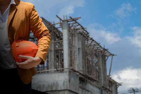 worker or engineer holding in hands helmet for workers security on background of new highrise apartment buildings and construction cranes on background.の写真素材