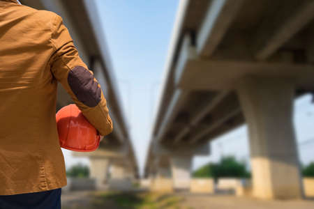 worker or engineer holding in hands orange helmet for workers security on the background of a new concrete bridgeの写真素材
