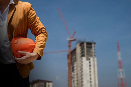 Worker or engineer holding in hands helmet for workers security on background of new highrise...