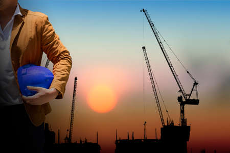 worker or engineer holding in hands helmet for workers security on background of new highrise...