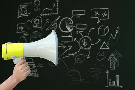 Human hand holding megaphone against blackboardの写真素材