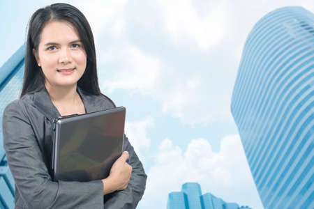 Businesswoman holding a laptop with cityscape on the backgroundのeditorial素材