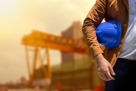 worker or engineer holding in hands helmet for workers security on background of new highrise...