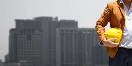 Torso engineer, worker or architect holding plastic helmet in hand on blurred city scape background.のeditorial素材