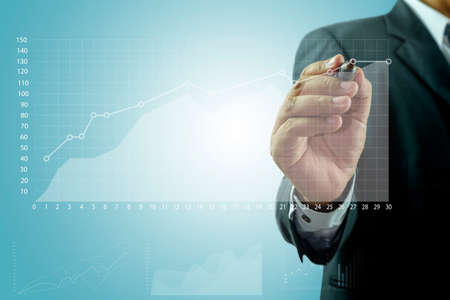 Businessman standing posture hand hold pen drawing graphics a growing graph over blue backgroundのeditorial素材