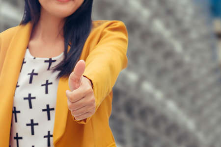 Asian business woman holding her thumb up outside in front of buildingの写真素材