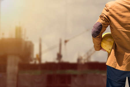 worker or engineer holding in hands helmet for workers security on background of new highrise apartment buildings and construction cranes on background.のeditorial素材