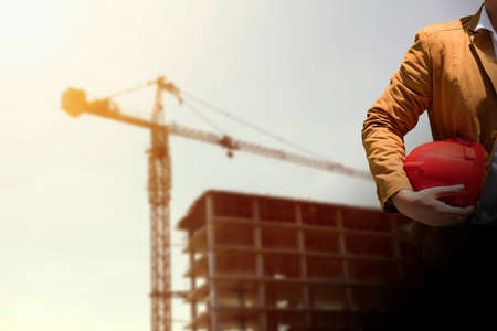 worker or engineer holding in hands helmet for workers security on background of new highrise apartment buildings and construction cranes on background.のeditorial素材