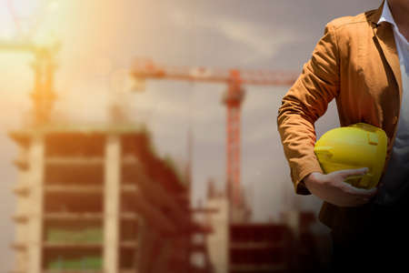 worker or engineer holding in hands helmet for workers security on background of new highrise...