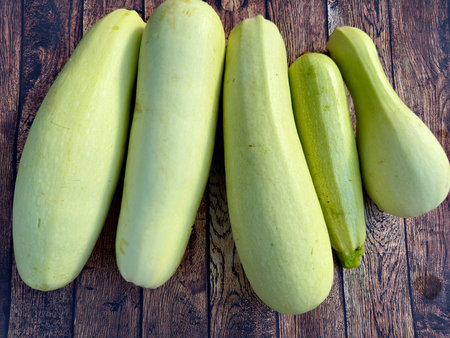 A group of fresh zucchini of different sizes lies on a brown wooden floor made of planks on a sunny day. Fresh zucchini on a cutting board. Whole zucchini fruits on a wooden backgrの写真素材