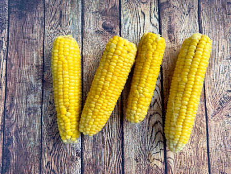 Freshly cooked delicious sweet corn on a wooden brown table. Boiled cobs of sweet corn on a wooden table. Appetizing healthy natural food. Top view of yellow cornの写真素材