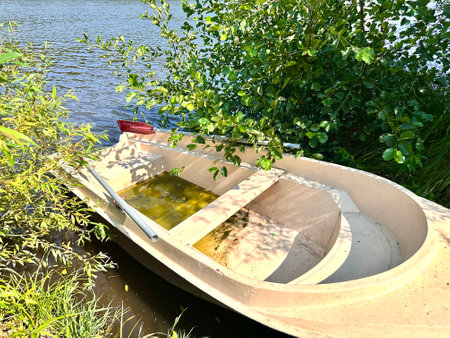 A rowing boat is moored on a grassy bank among green trees on a sunny summer day against a forest background. An empty boat on the shore of a lake in the midst of beautiful greenの写真素材