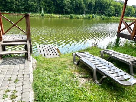 A recreation center with a separate divided relaxation area with deck chairs and a wooden pier on the river bank in the middle of the forest. The concept of recreation in natureの写真素材