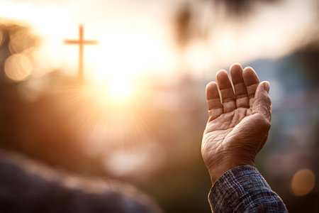 Open hand showing spiritual gesture while reaching for the light of the setting sun, symbolizing prayer, worship, and devotion with a blurred Christian cross in the backgroundの写真素材