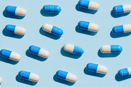 Blue and white pharmaceutical capsules arranged in a repeating pattern on a soft blue background, conveying medication, dosage control, healthcare and pharmaceutical industry themesの写真素材