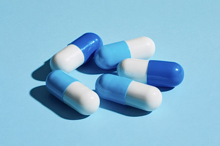 Various blue and white medicine capsules laying scattered on a vibrant light blue background,...
