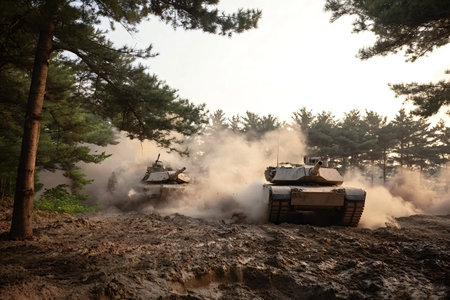 M1 abrams main battle tanks maneuvering through a muddy forest, kicking up dust and smoke during military training, representing power, combat readiness, and defense operationsの写真素材