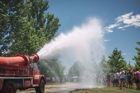 Red vintage fire truck spraying a powerful jet of water onto the street, refreshing a cheering crowd...